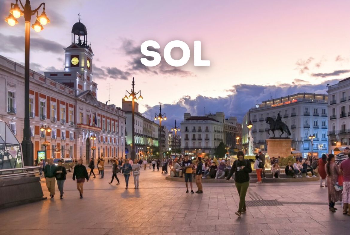Vista panorámica de la Puerta del Sol al atardecer, destacando el icónico edificio del Reloj y la palabra "SOL", un punto clave para invertir en el barrio Sol de Madrid.